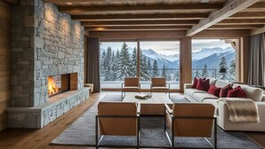 A cozy living room with a stone fireplace, wooden beams, a sofa with red cushions, and a view of snow-covered mountains.