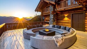 A log cabin with a circular outdoor seating area, a fire pit, and a view of the sunset.