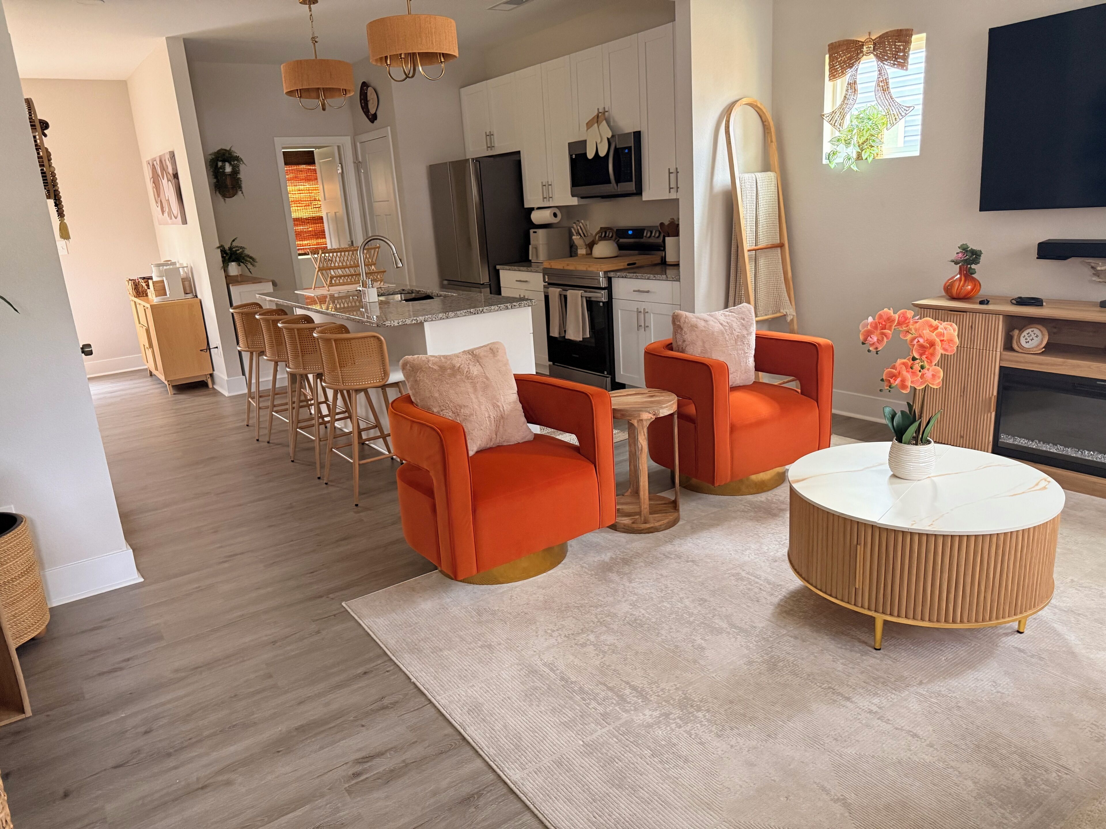 A modern living room with orange armchairs, a round coffee table, and a TV mounted on the wall.