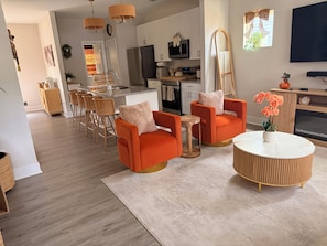 Una sala de estar moderna con sillones naranjas, una mesa de centro redonda y un televisor montado en la pared.