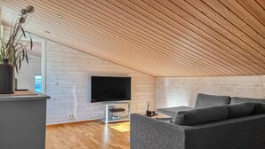 En moderne stue med et fladskærms-TV, en grå sofa, trægulv og et loft med trælameller.