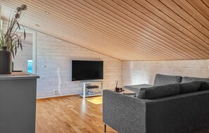 A modern living room with a flat-screen TV, grey sofa, wooden flooring, and a ceiling with wooden slats. - Awesome home in Uddevalla with house sea view (Uddevalla)