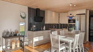Et moderne køkken med en central ø, hvide skabe og et spiseområde med hvide stole.