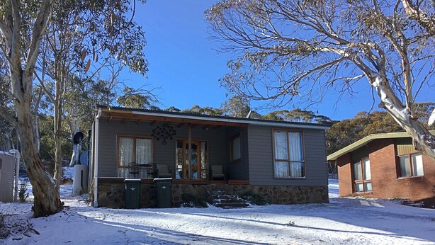 A two-story house with a stone foundation, a porch with chairs, and a satellite dish. - Cosy Cottage at Anglers Reach close to Lake Eucumbene and Selwyn Snow Resort (Anglers Reach)