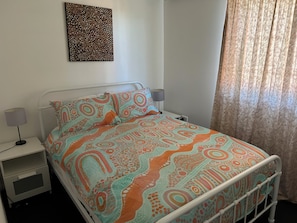 A bed with patterned bedding, a bedside table with a lamp, and a wall art piece.