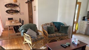 A living room with wicker furniture, a wooden coffee table, and a dining area with a table and chairs. - Cosy Cottage at Anglers Reach close to Lake Eucumbene and Selwyn Snow Resort (Anglers Reach)