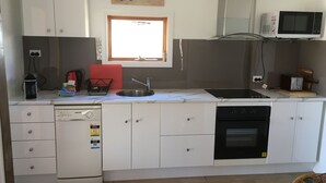 A compact kitchen with a dishwasher, oven, microwave, and a window above the sink. - Cosy Cottage at Anglers Reach close to Lake Eucumbene and Selwyn Snow Resort (Anglers Reach)