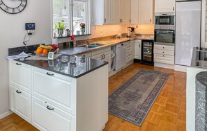 Eine moderne Küche mit weißen Schränken, einer Granit Arbeitsplatte, einem eingebauten Backofen und einem großen Fenster.
