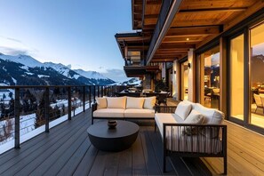 A wooden deck with a sofa and a round table, overlooking a snowy mountain range.