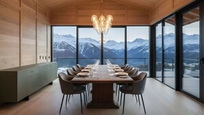 Ein Essbereich mit Holztisch, gedeckt für sechs Personen, großen Fenstern mit Bergblick und einer modernen Pendelleuchte.