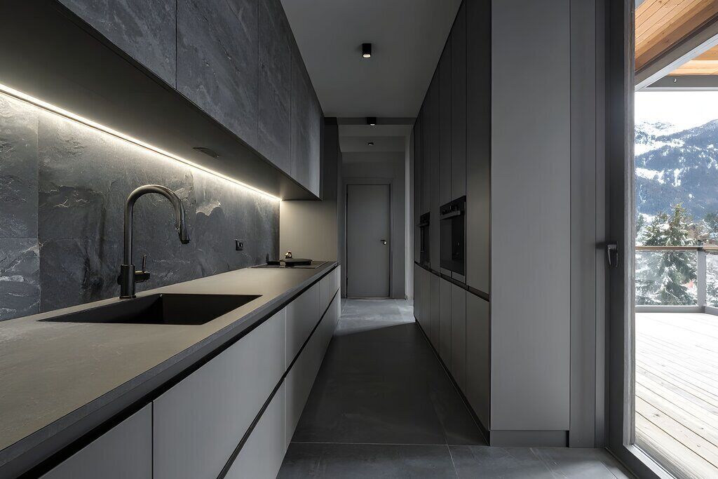 A modern kitchen with a long countertop, a sink, and a backsplash.