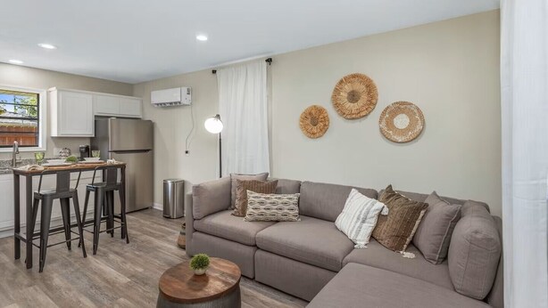 En moderne stue med sofa, sofabord og et køkkenområde med køleskab og barstole.