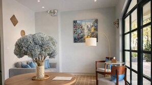 Una sala de estar moderna con una mesa redonda de madera, un sofá con cojines azules, un ventanal con vistas y un cuadro en la pared.