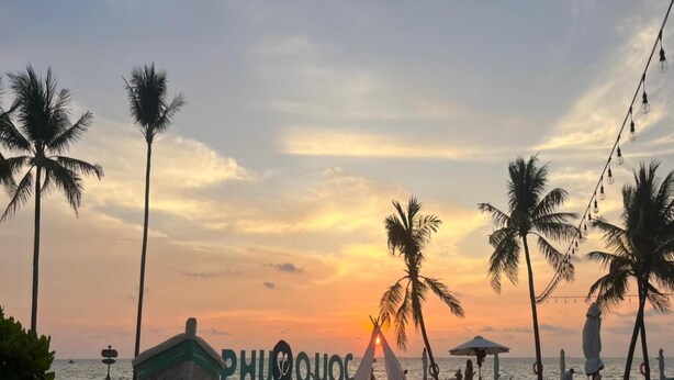 Una playa con palmeras, una carpa y un letrero que dice 'PHUQUOC'.