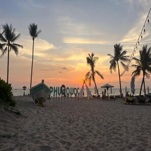 Une plage bordée de palmiers, une tente et un panneau indiquant « PHUQUOC ».