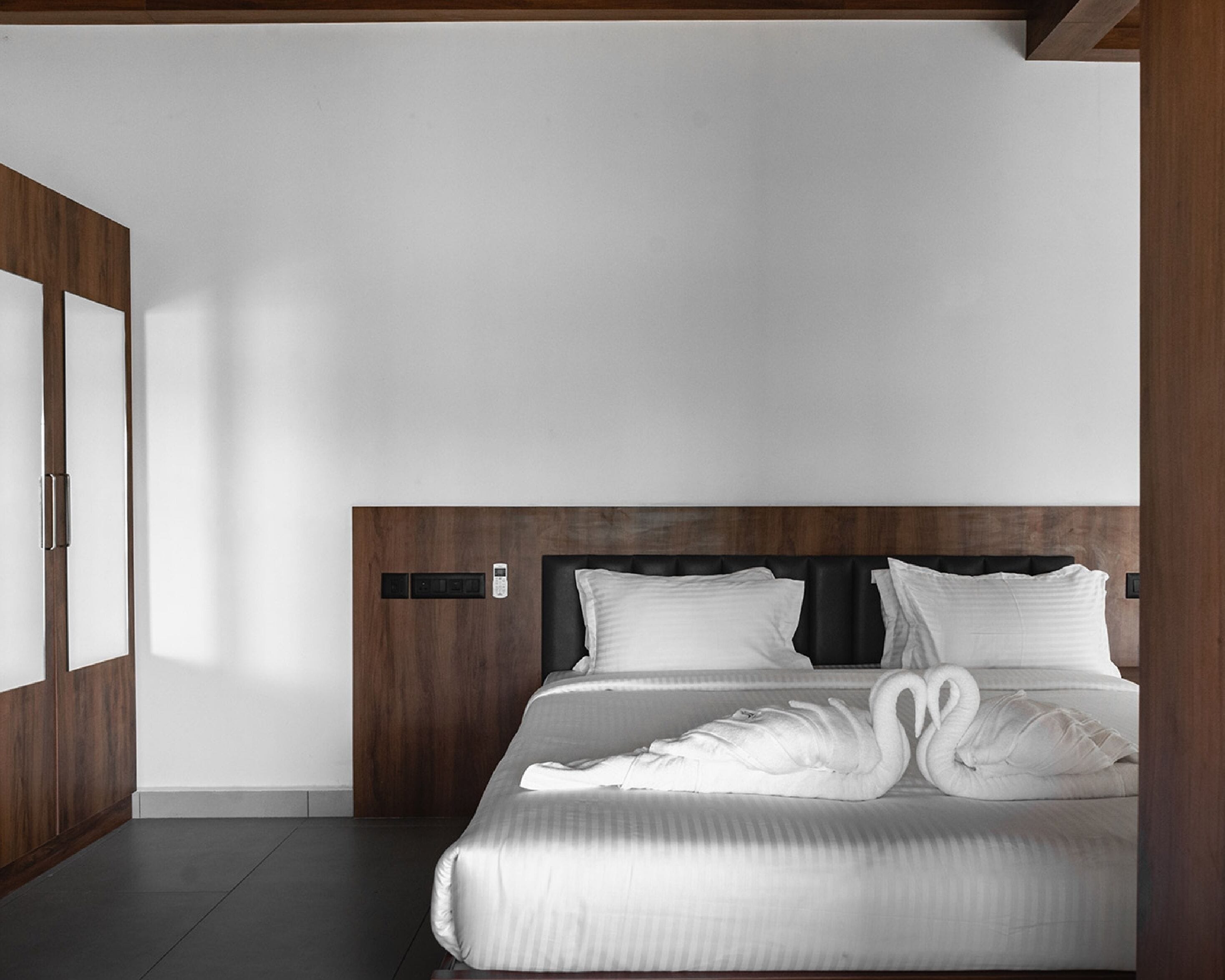 A modern hotel room with a large bed, wooden headboard, and a built-in control panel.