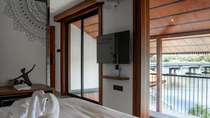 Un dormitorio con cama, televisor de pared, ventana grande y vistas a un espacio exterior.