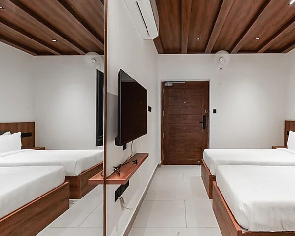 A hotel room with two beds, a TV mounted on the wall, a wooden door, and a ceiling with wooden beams.