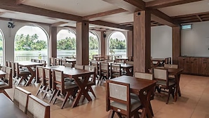 Un amplio comedor interior con mesas y sillas de madera, ventanas grandes y una pizarra en la pared.