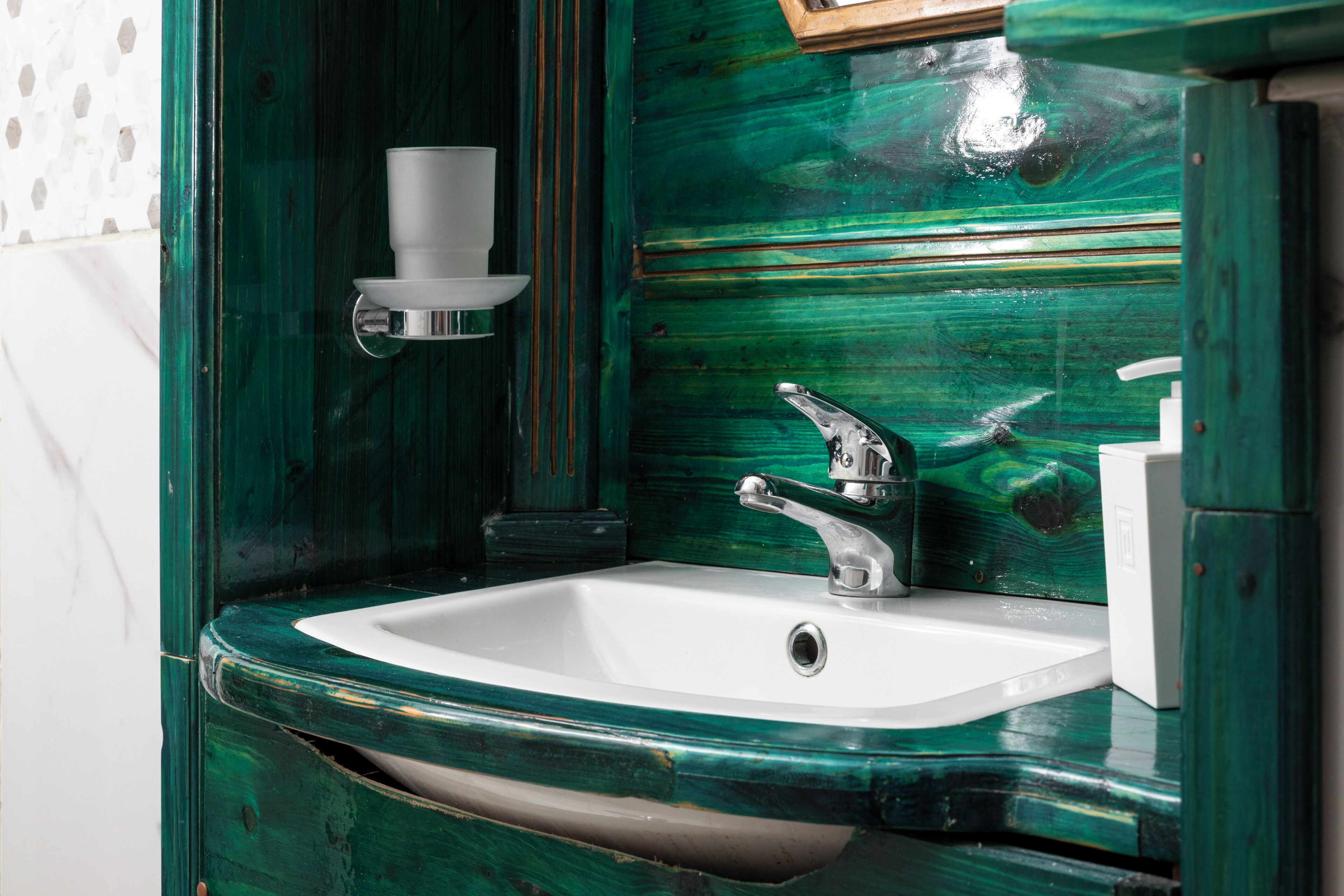 A bathroom with a white sink, a chrome faucet, and a green wall.
