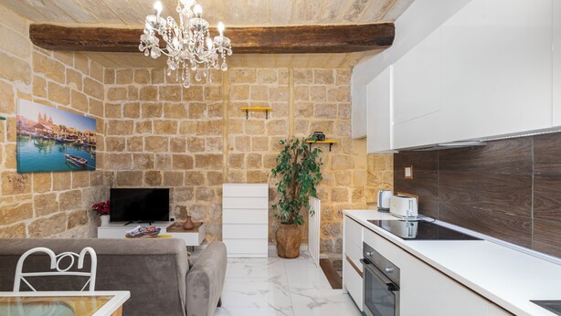 A modern kitchen with white cabinets, a built-in oven, and a stone wall backdrop. - Chic Comfy 1BR Maisonette Valletta Area (Floriana)
