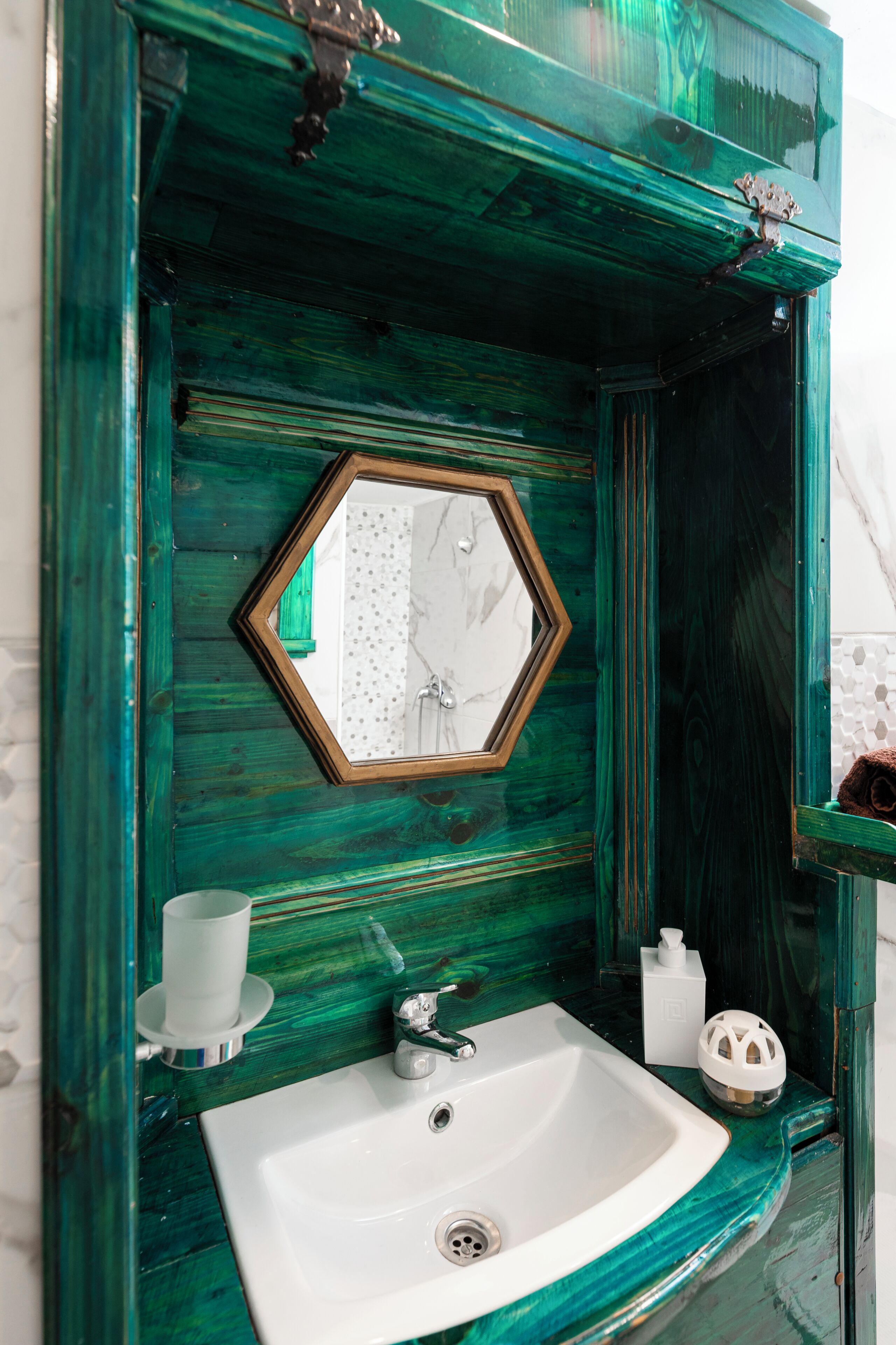 A bathroom with a green wooden vanity, a white sink, and a mirror with a hexagonal frame.