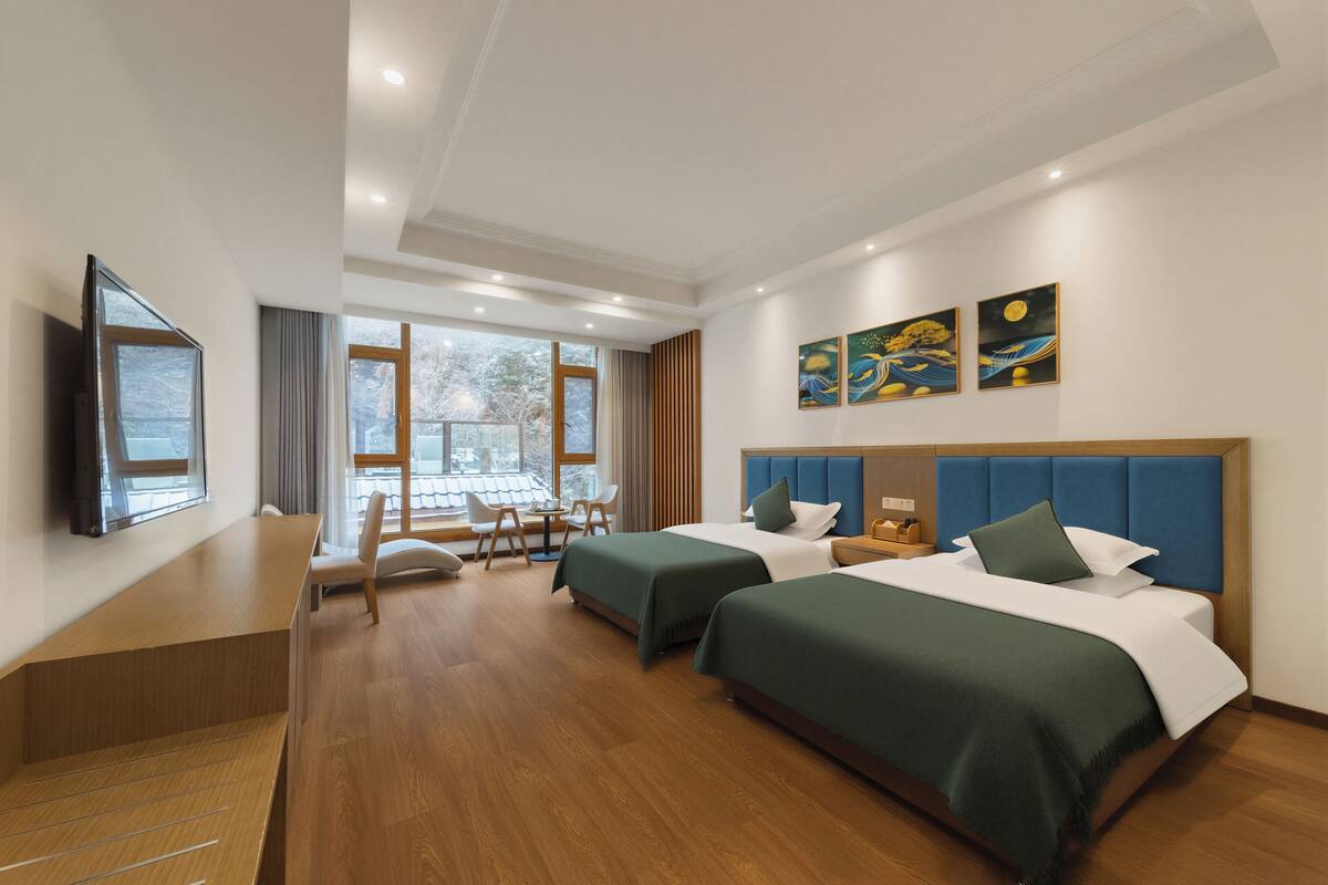 A hotel room with two beds, a desk, a TV, and artwork on the wall.