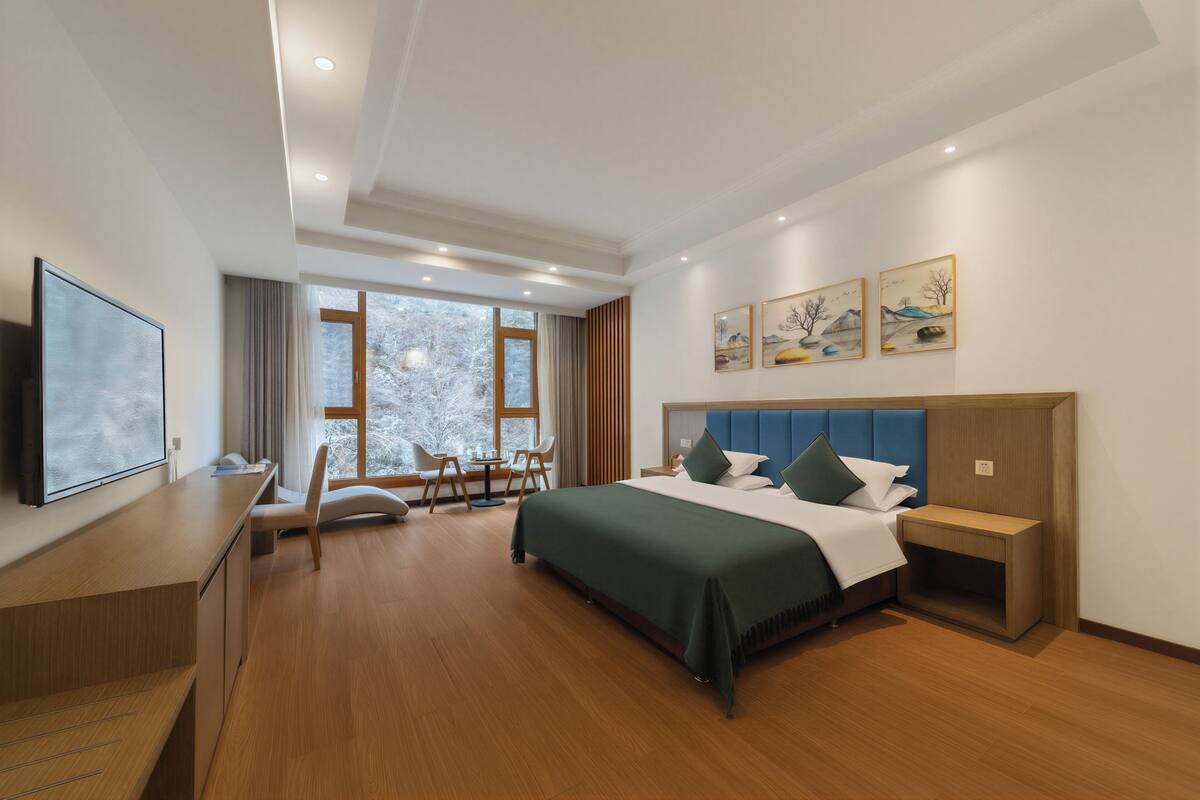 A modern hotel room with a large bed, a desk, a chair, and a TV.