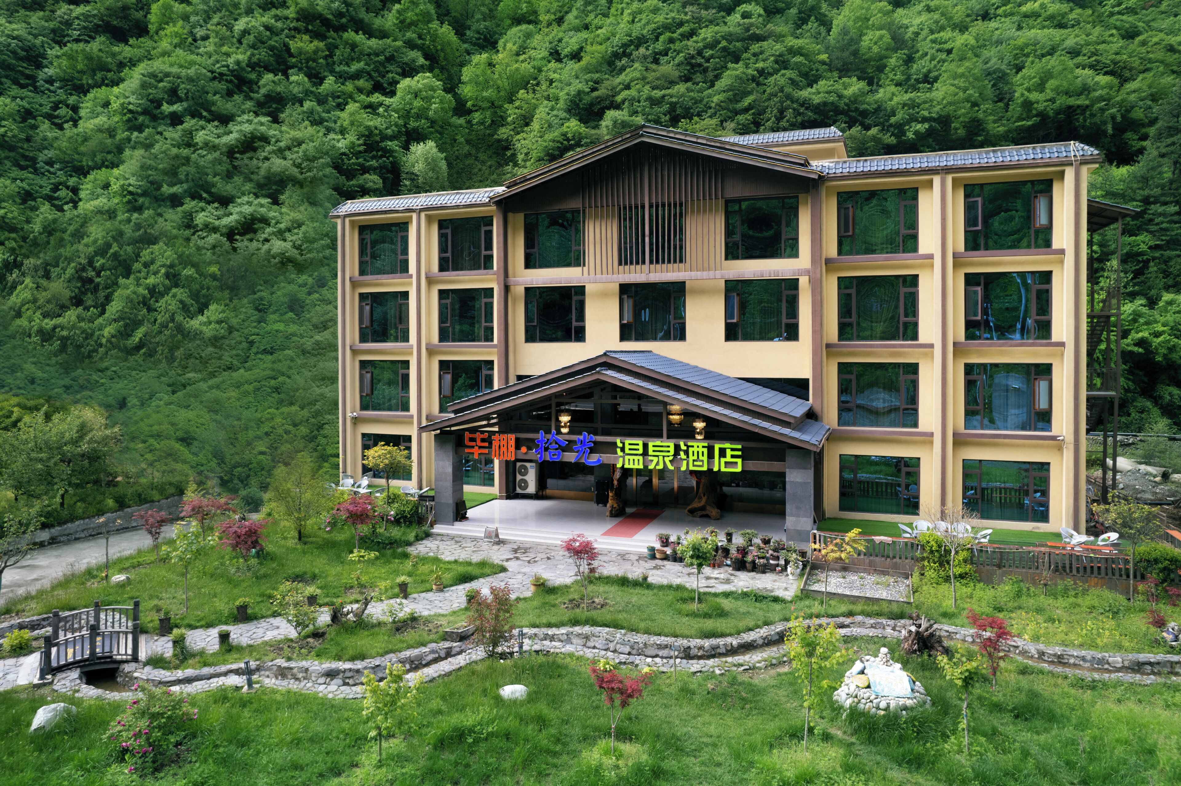 A multi-story hotel with a modern design, featuring a central entrance, outdoor seating, and a landscaped garden.