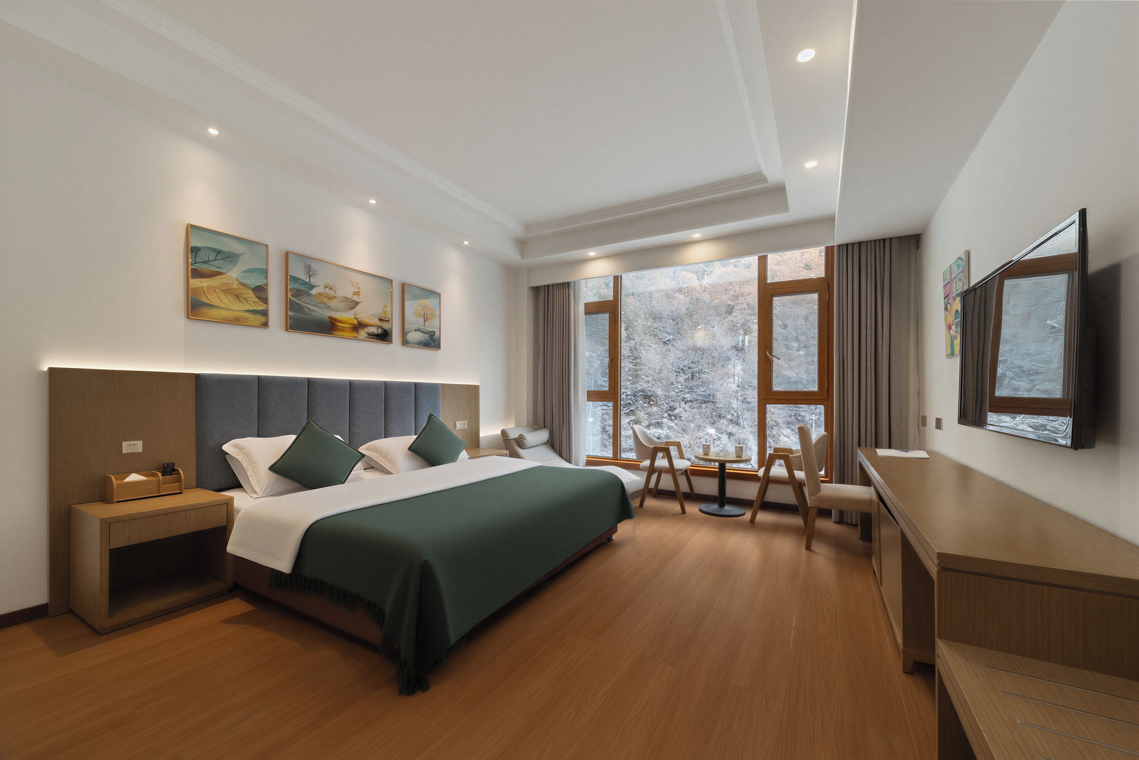 A hotel room with a bed, bedside table, desk, chair, and large windows.