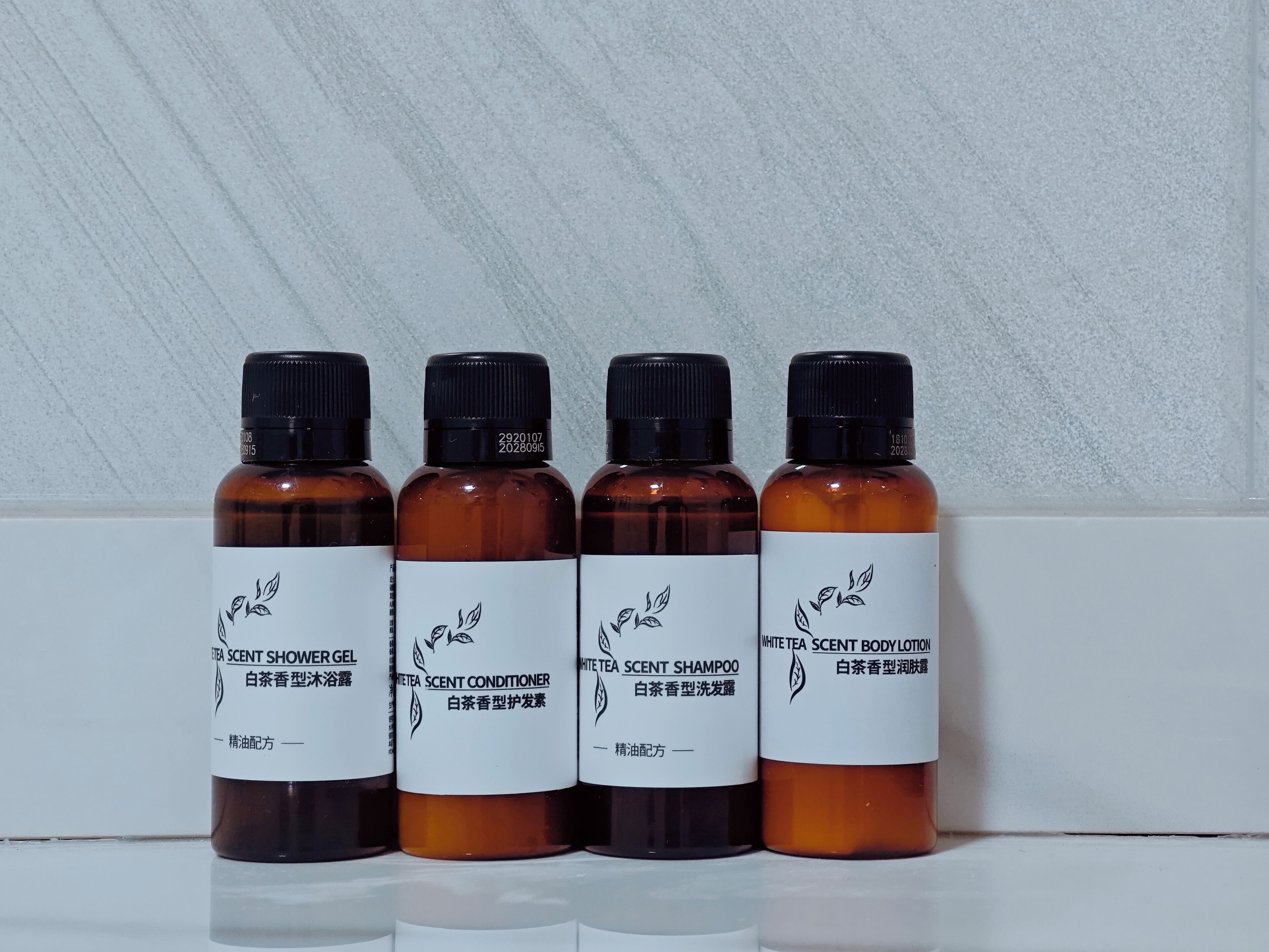Quatre flacons de produits parfumés au thé blanc, placés sur une surface réfléchissante.