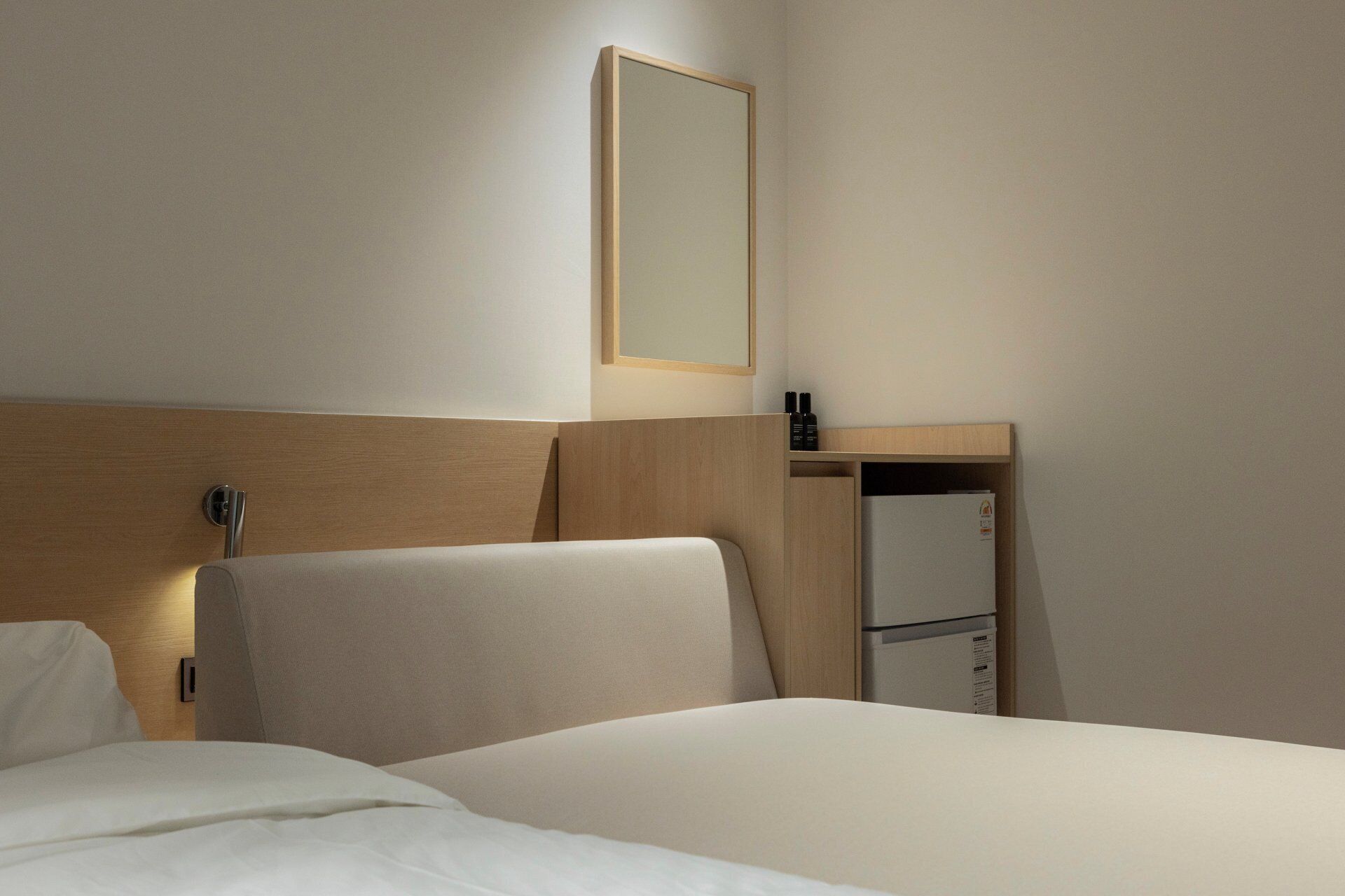 Una habitación de hotel con una cama, un cabecero de madera, una mesita de noche con espejo y un pequeño estante con objetos.