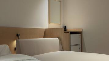 Una habitación de hotel con una cama, un cabecero de madera, una mesita de noche con espejo y un pequeño estante con objetos.