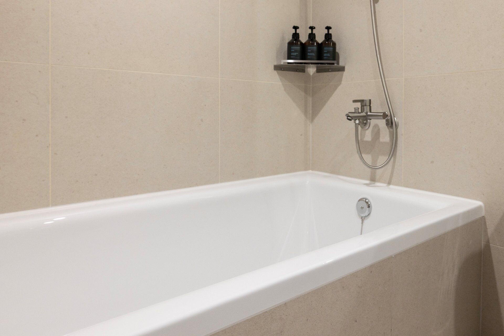 A white bathtub with a handheld showerhead and a wall-mounted faucet.