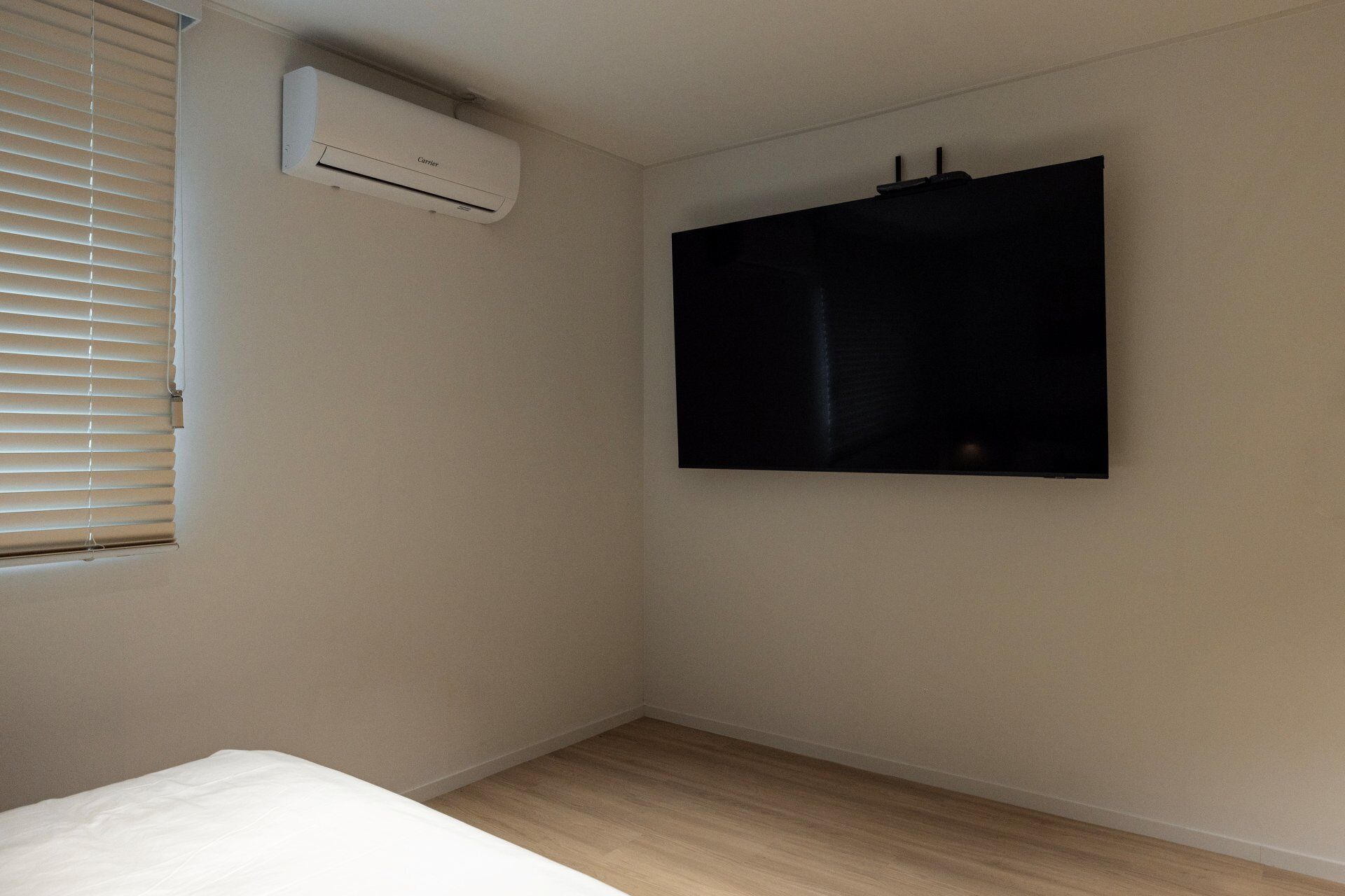 Una habitación con una cama, aire acondicionado instalado y un televisor en la pared.