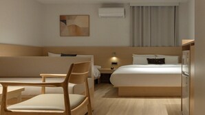 Habitación de hotel con cama, escritorio, silla, mesita de noche, lámpara y equipo de aire acondicionado.