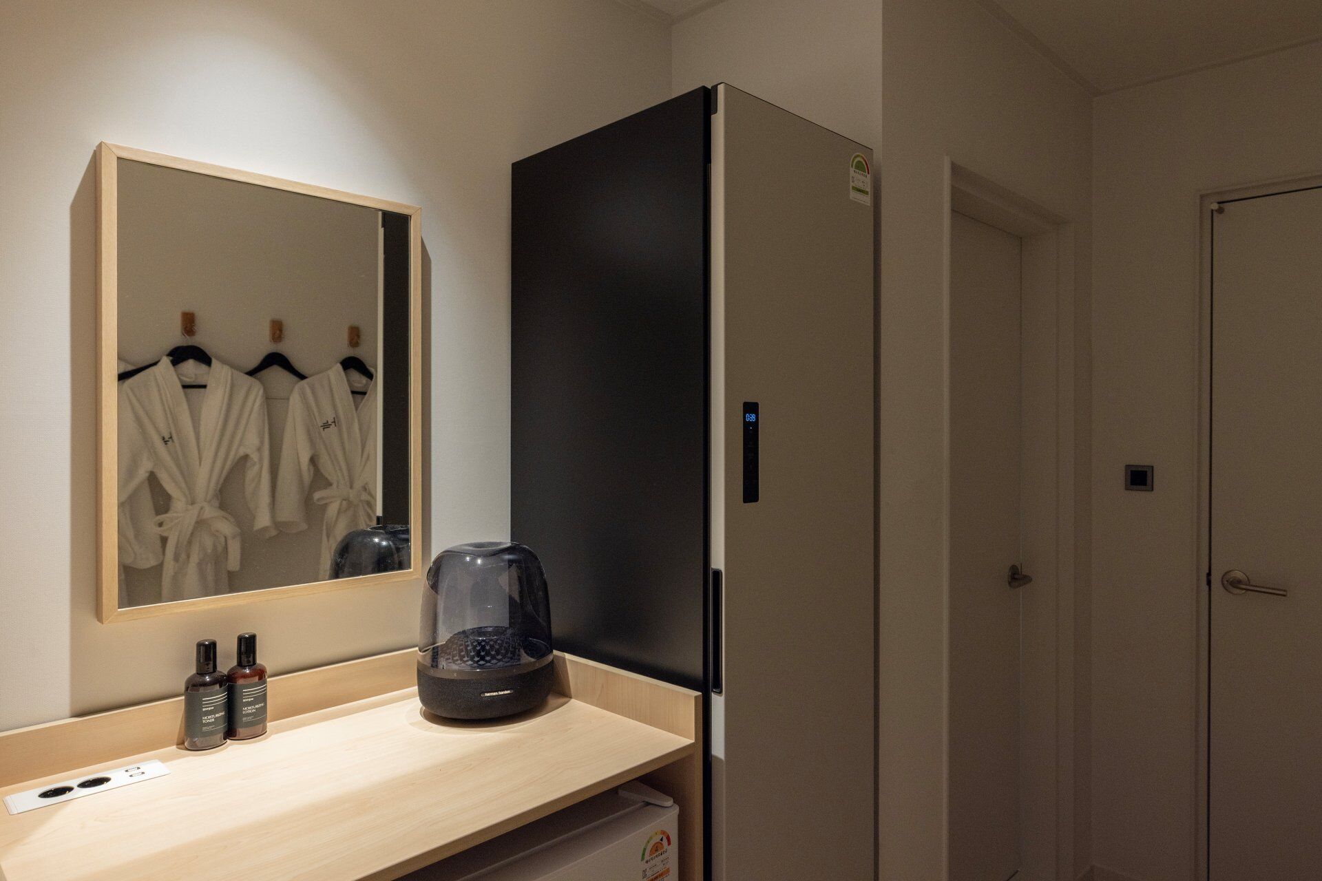 Habitación de hotel con espejo, cafetera, refrigerador y puerta.