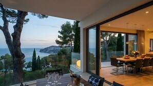 Un coin repas avec vue sur la mer, une table dressée avec des verres et une bouteille, et un intérieur moderne.