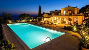 Une piscine avec des chaises longues, une grande maison dotée de nombreux balcons et une vue sur la mer.