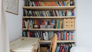 A bookshelf filled with books, a small table, and a chair in a room with white walls. - Serene 1BD by London Fields and Victoria Park (Greater London)
