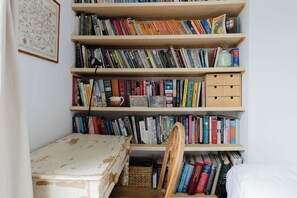 A bookshelf filled with books, a small table, and a chair in a room with white walls. - Serene 1BD by London Fields and Victoria Park (Greater London)
