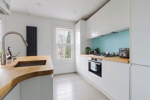 A modern kitchen with white cabinetry, a wooden countertop, a built-in oven, and a window with a view of trees. - Serene 1BD by London Fields and Victoria Park (Greater London)
