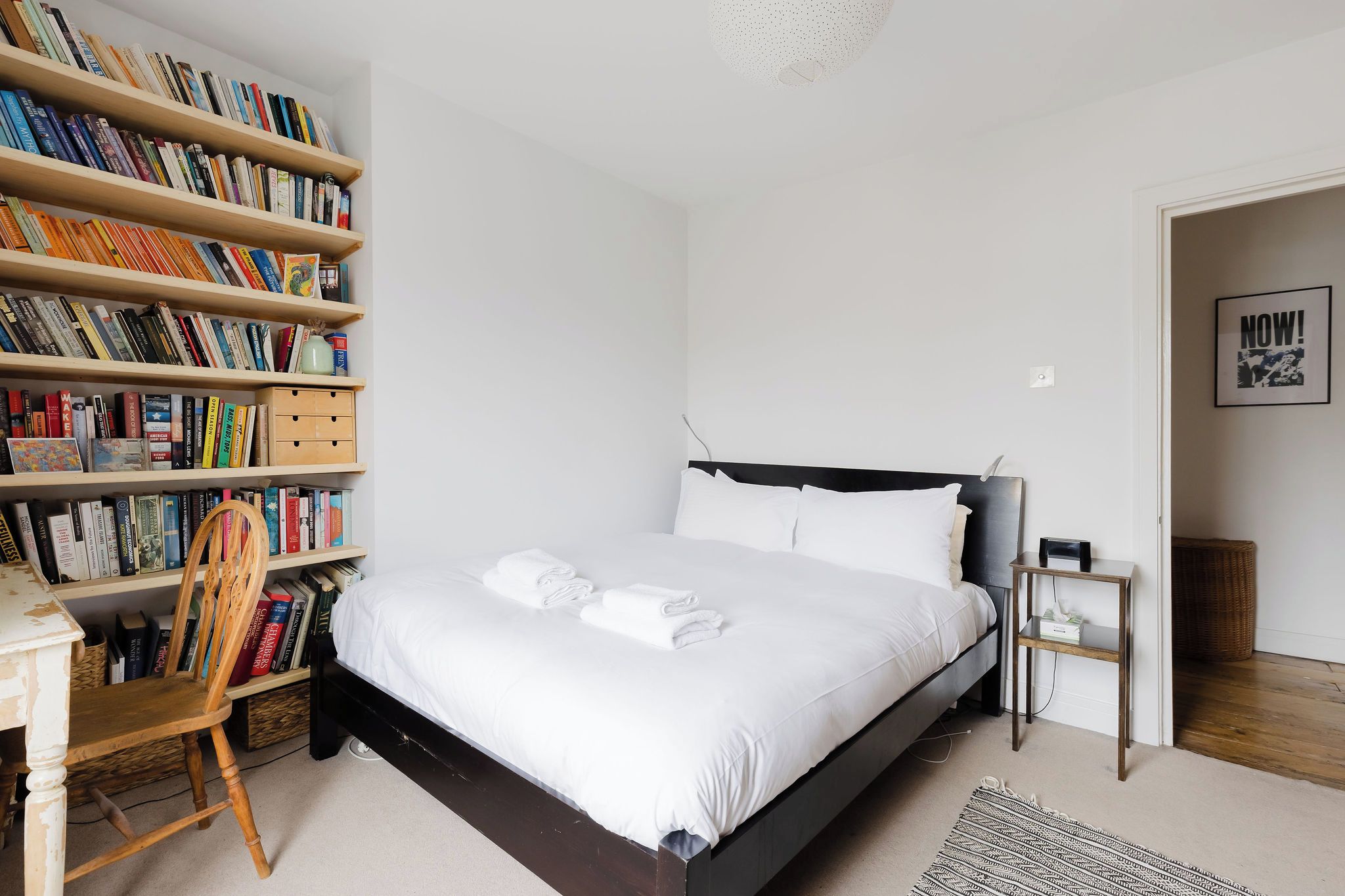 Een slaapkamer met een bed, een boekenkast, een stoel en een klein nachtkastje.