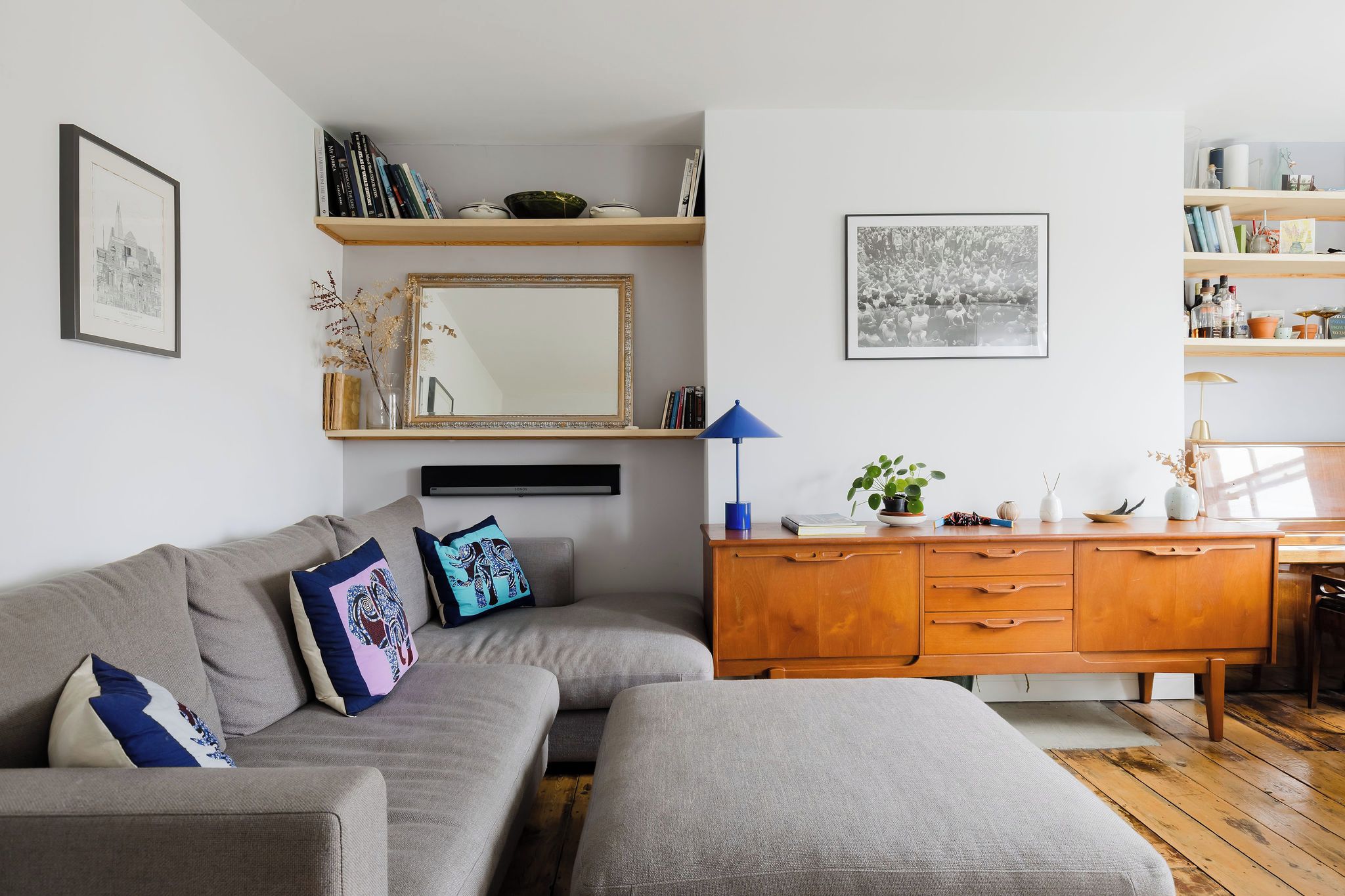 Una sala de estar con un sofá gris, un aparador de madera y un televisor de pantalla plana.