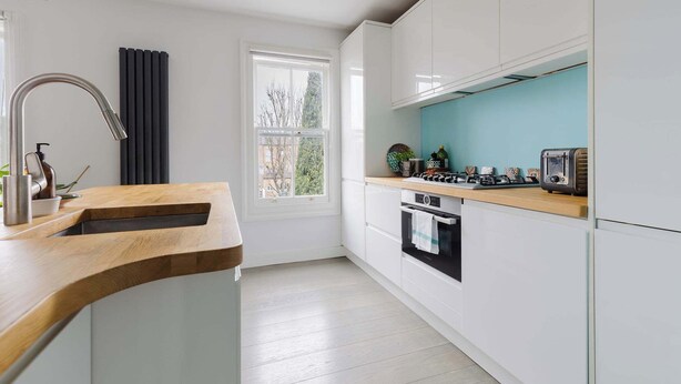 A modern kitchen with white cabinets, a wooden countertop, a window, and a view of the outdoors. - Serene 1BD by London Fields and Victoria Park (Greater London)