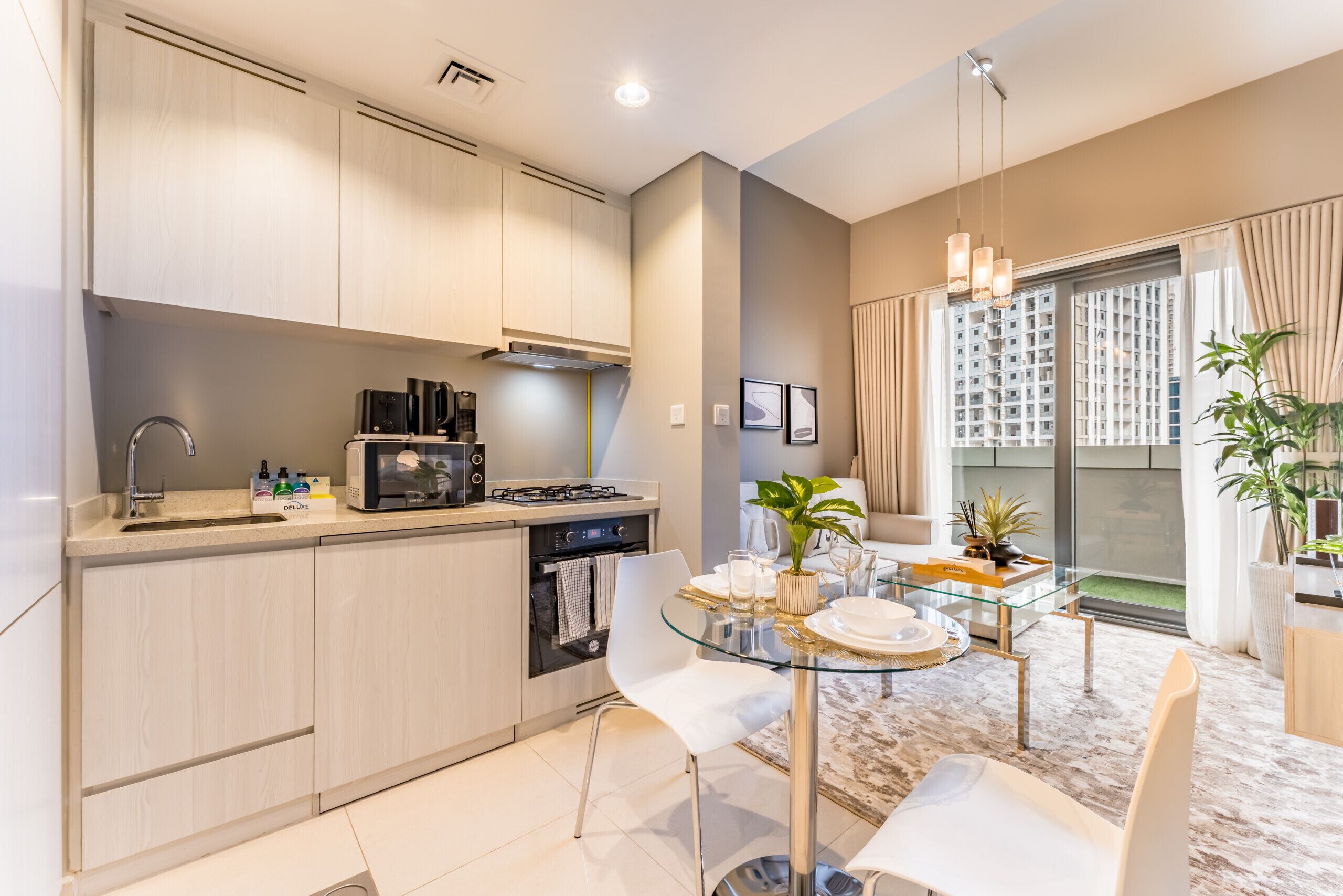 Une cuisine moderne avec un coin repas, comprenant une table en verre, des chaises blanches et une vue sur un immeuble d’habitation.