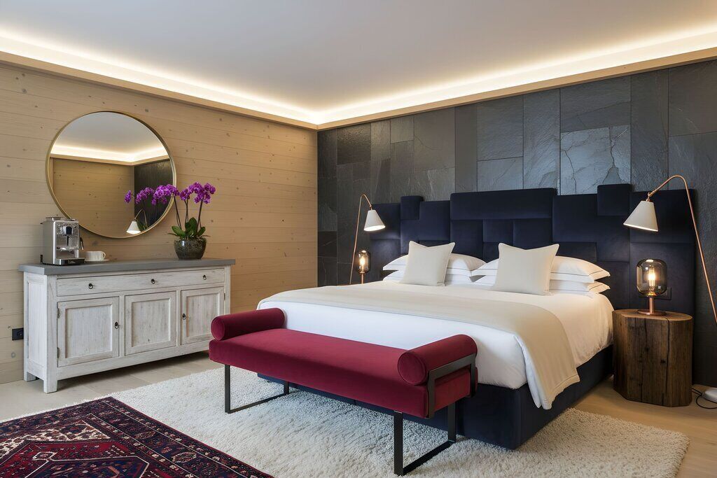 Une chambre à coucher moderne avec un grand lit, une commode en bois, un banc rouge et un miroir rond.