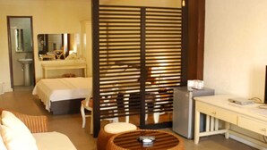 Une chambre d’hôtel comprenant un lit, un bureau, un réfrigérateur, des meubles en osier et une cloison.