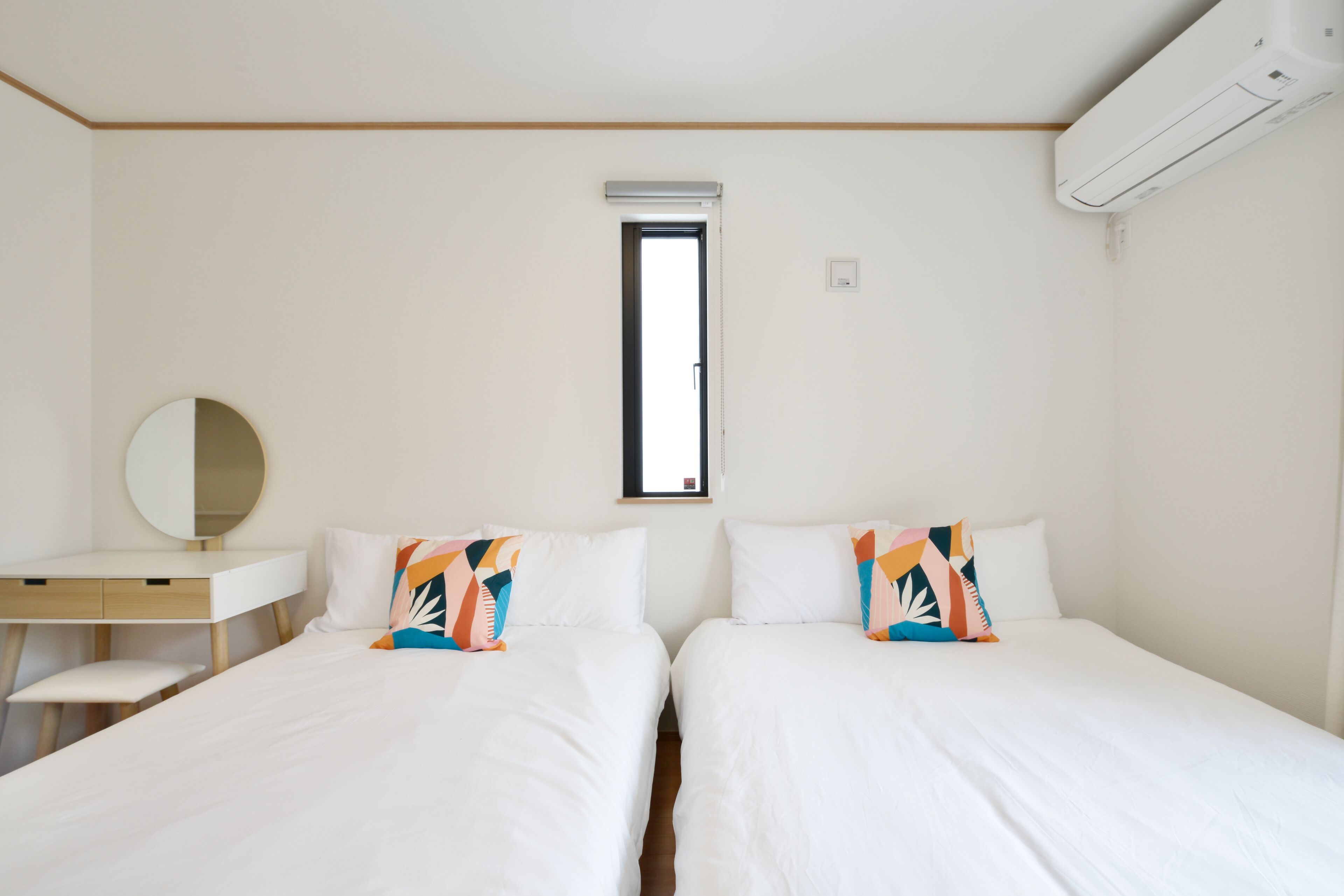 A room with two beds, a desk, a mirror, and an air conditioning unit.