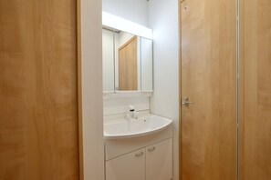 Een badkamer met een witte wastafel, spiegel en houten deur.